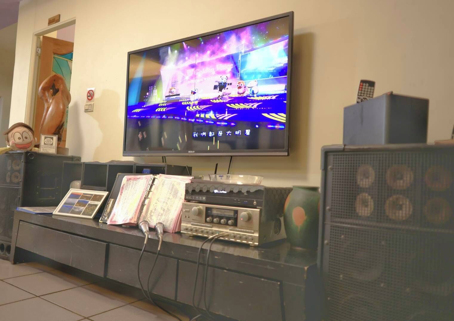 A television mounted on a wall displaying a colorful show, a sound system, and a decorative owl figure.