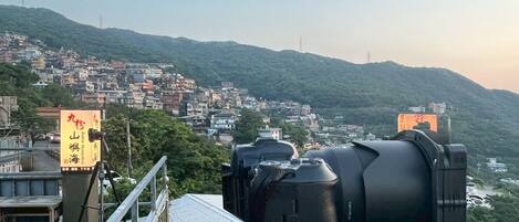 A camera on a balcony overlooking a densely packed hillside town with visible buildings and infrastructure.