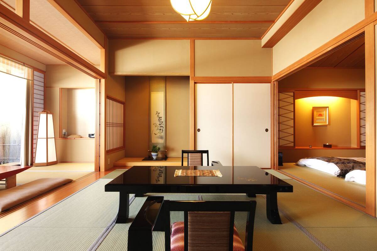 Ein traditioneller japanischer Raum mit Tatami-Boden, einem niedrigen Tisch, einem Bett und Schiebetüren.