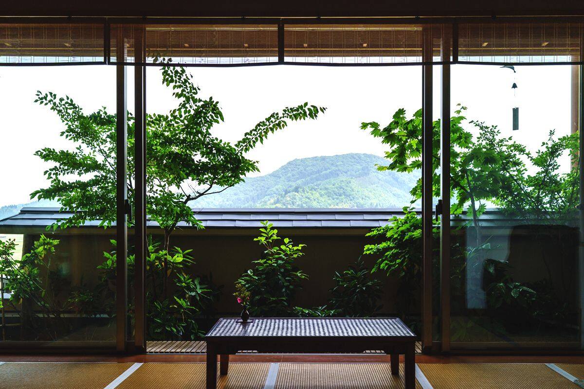 Ein Zimmer mit großen Fenstern, einem Tatami-Boden, einem niedrigen Tisch und Blick auf einen Berg.