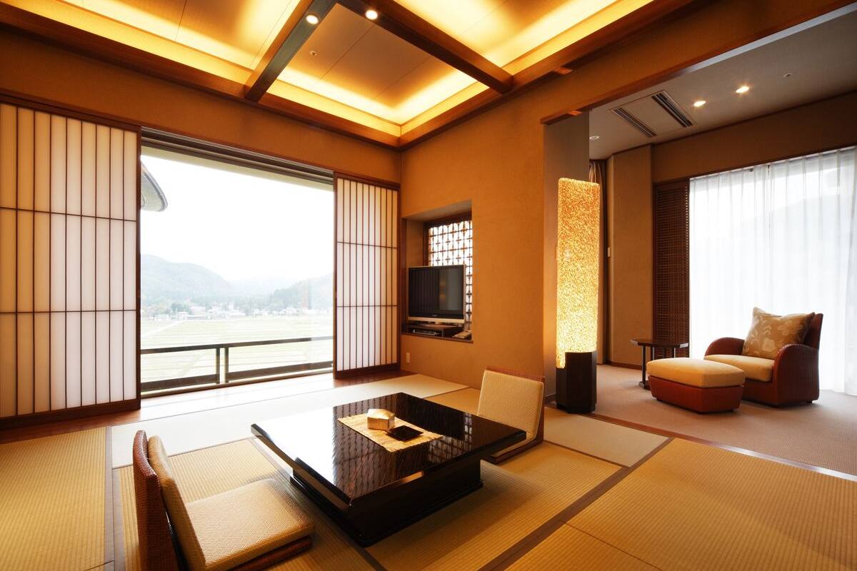 Ein traditionelles japanisches Wohnzimmer mit Tatami-Böden, einem niedrigen Tisch mit Kissen, einem Fernseher und einer Couch mit Kissen.