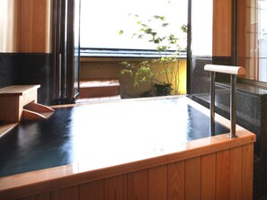 A hot spring bath with wooden benches and a view of a building and trees outside. - Shiratama no yu KAHOU Bettei Koshinosato (Shibata)