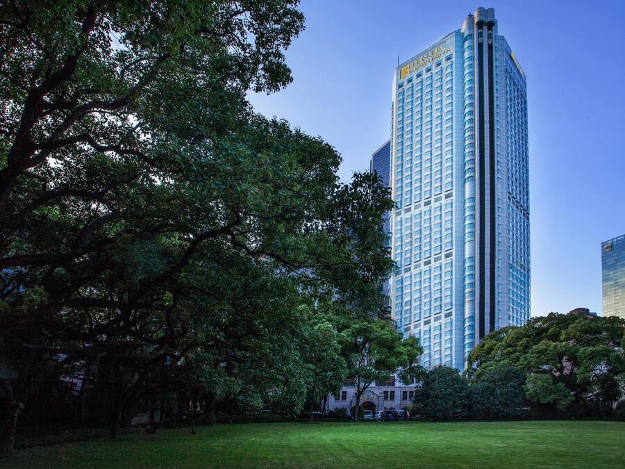 A tall building with a modern design, surrounded by lush green trees and a well-maintained lawn.