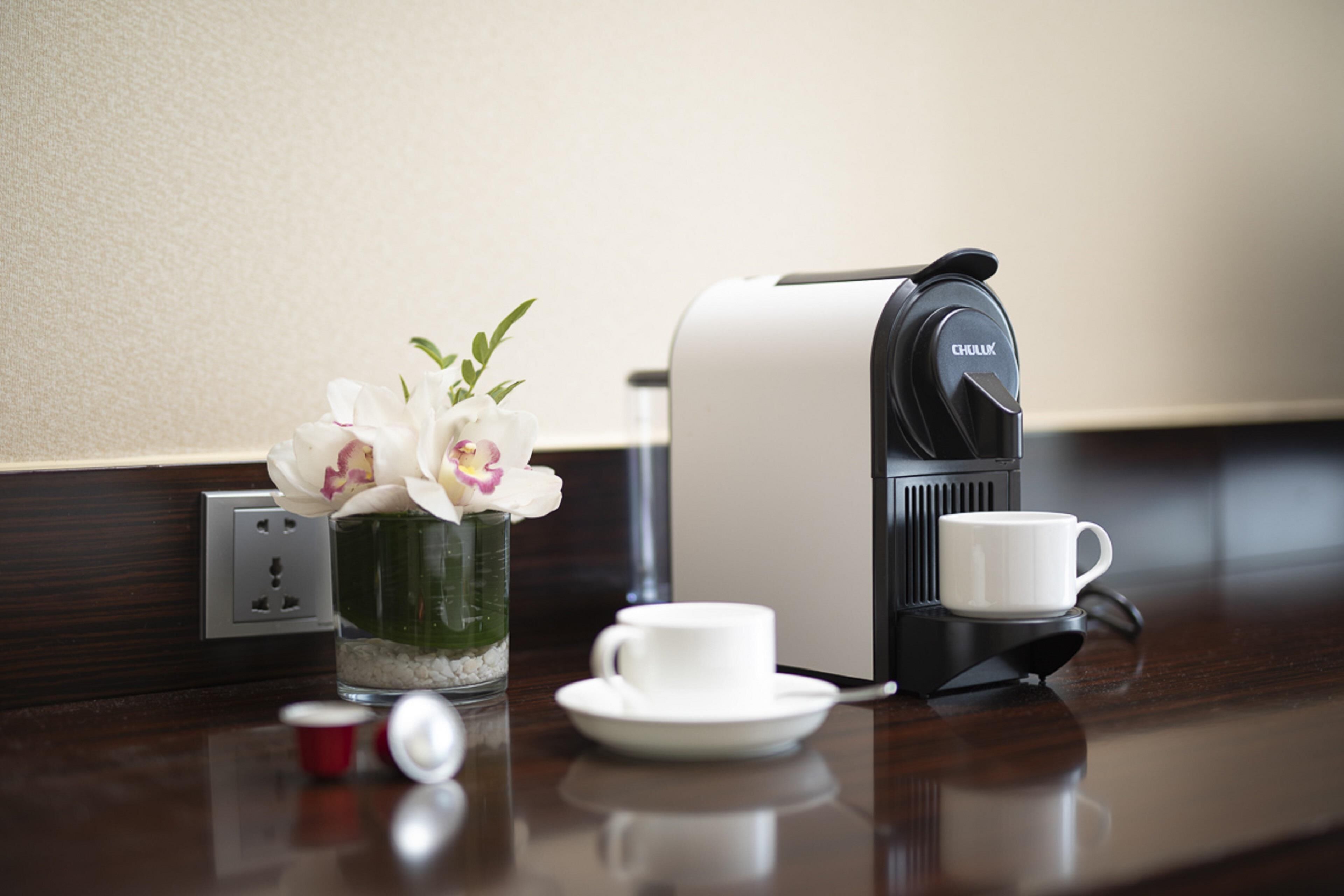 Une machine à café, une tasse, une soucoupe et un petit vase avec des fleurs sur une table en bois.