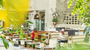 A restaurant with multiple seating areas, including booths and tables, with a decorative wall and a plant in the foreground. - The Kunlun Jing An (Shanghai)