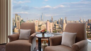 A hotel room with two armchairs, a small table with a fruit bowl, and a view of a city skyline. - The Kunlun Jing An (Shanghai)
