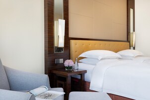 A hotel room with a bed, a bedside table with a vase of flowers, a chair, and a large mirror.