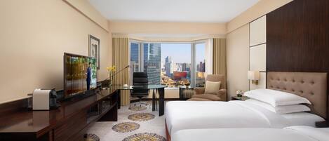 A hotel room with a large bed, a desk with a computer, a chair, and a view of the city skyline.