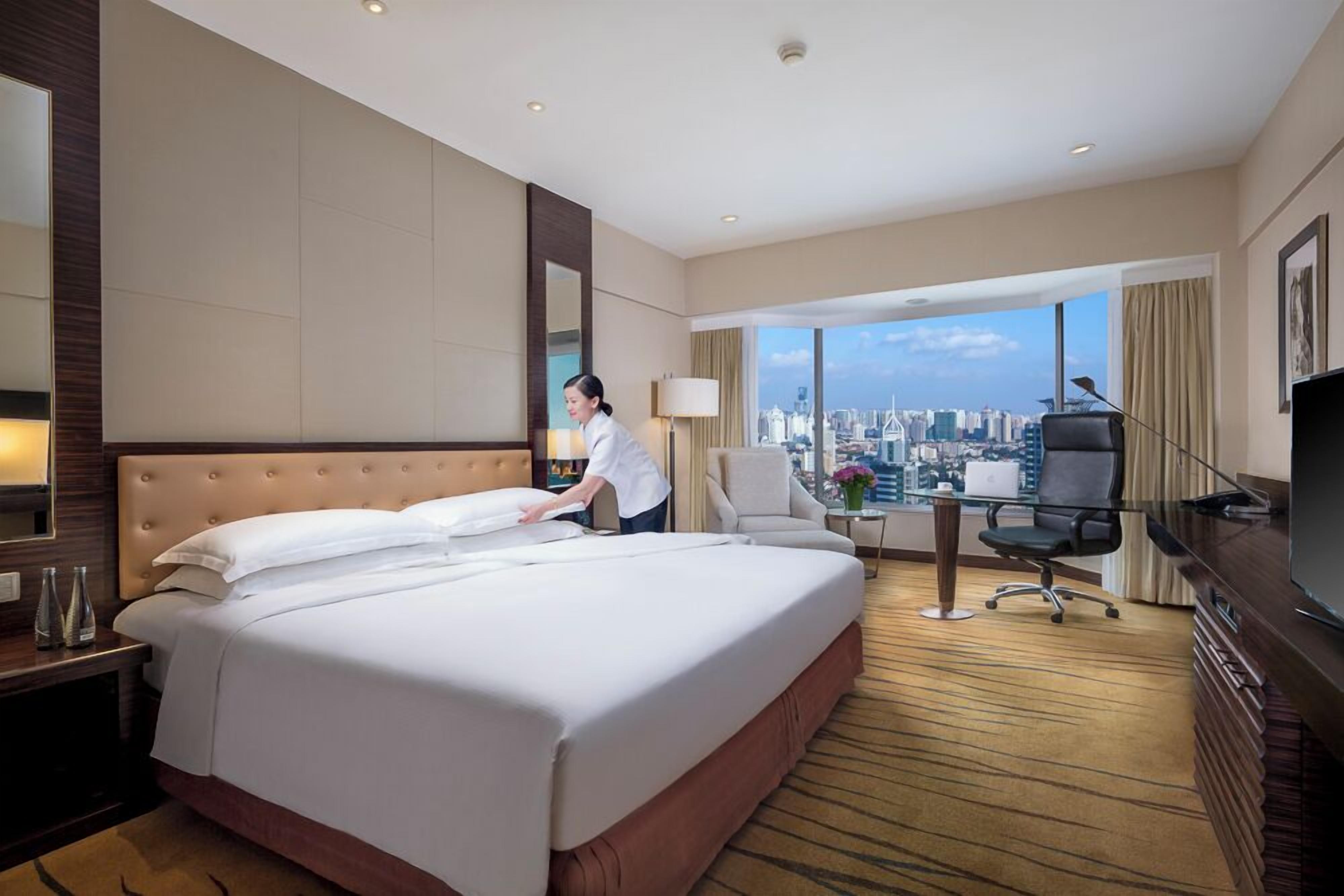 Habitación de hotel con una cama grande, un escritorio, una silla, un televisor y vistas a la ciudad.