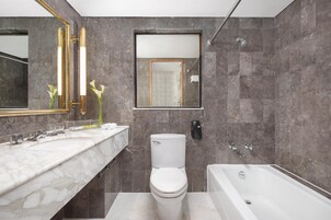 A modern bathroom with a marble vanity, a toilet, and a bathtub.