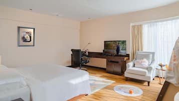 A hotel room with a bed, desk, chair, television, and a small table with a bowl of fruit.