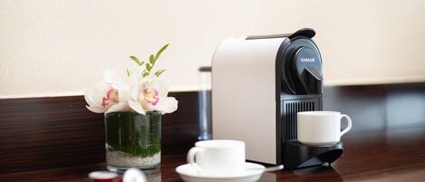 A coffee maker, a cup, and a vase with flowers on a wooden table.