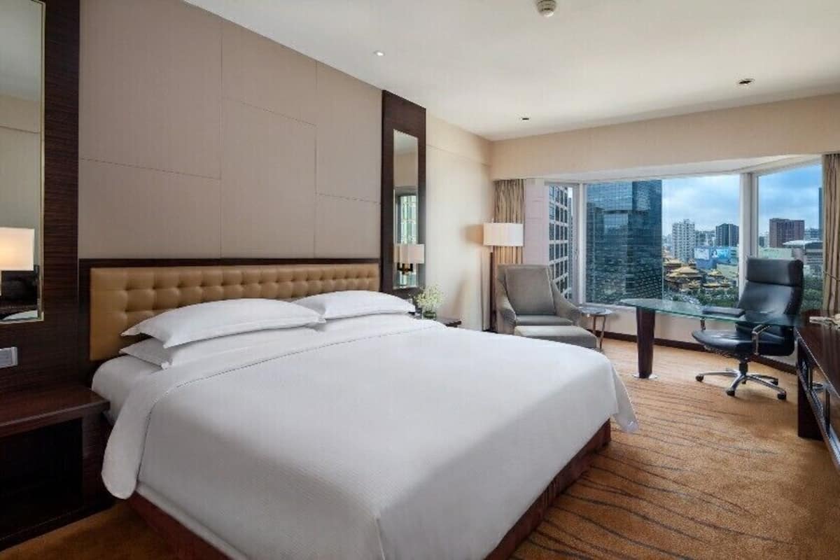 A hotel room with a large bed, a desk with a computer, a chair, and a television.