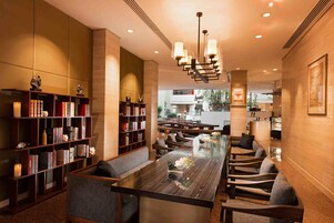 A modern library with bookshelves, a long table, and comfortable seating.