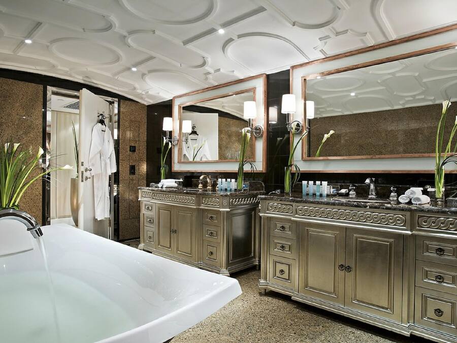 A luxurious bathroom with a large freestanding bathtub, double vanity with mirrors, and decorative plants.