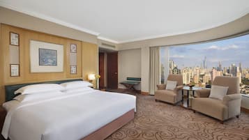Habitación de hotel con una cama grande, dos sillones, una mesita y vistas a la ciudad.