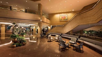 A spacious lobby with a central seating area, a staircase, and a large painting on the wall.