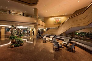 A spacious lobby with a central seating area, a staircase, and a large painting on the wall.