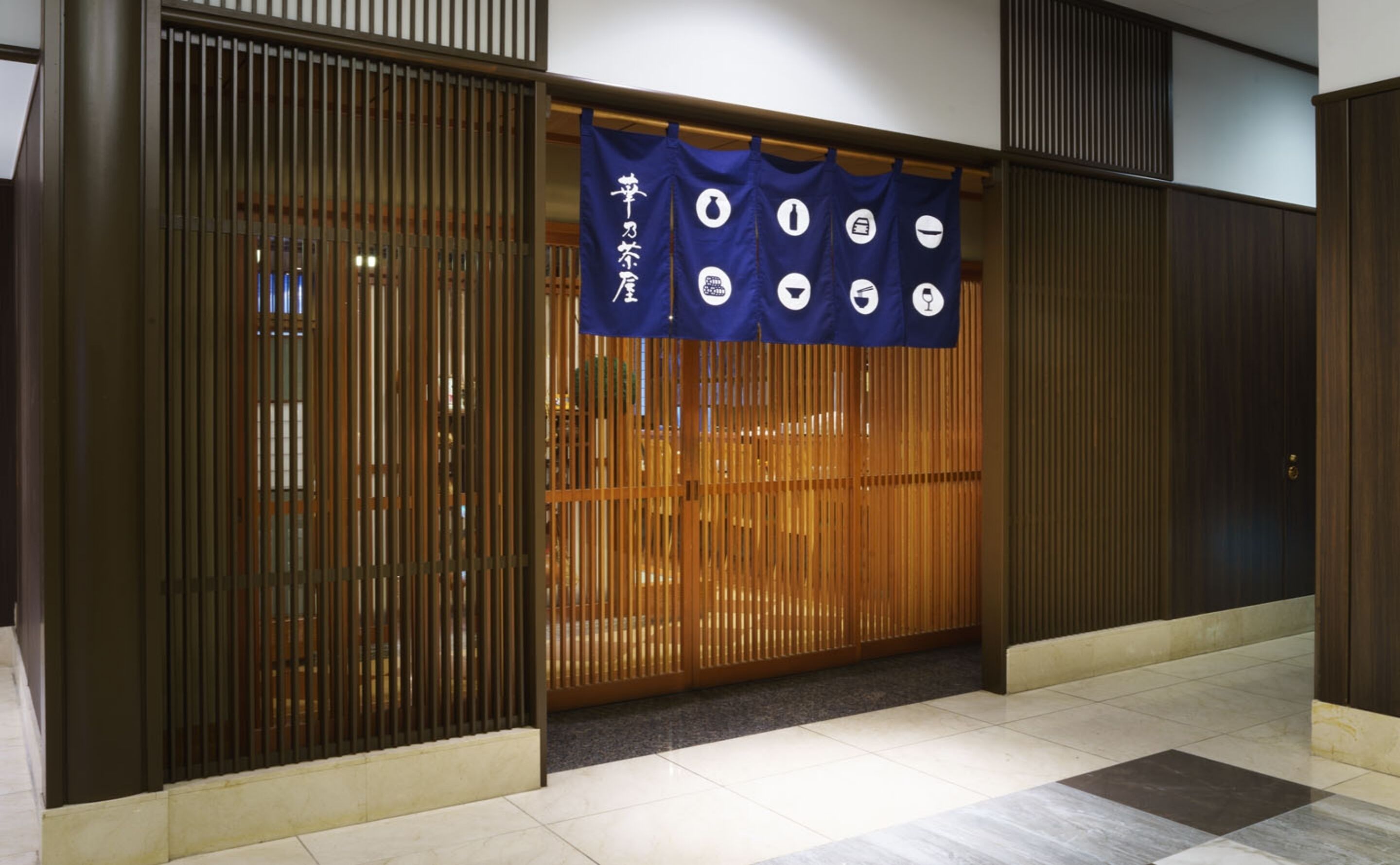 Une entrée de style japonais traditionnel, avec des portes coulissantes et une bannière bleue suspendue ornée d’icônes.
