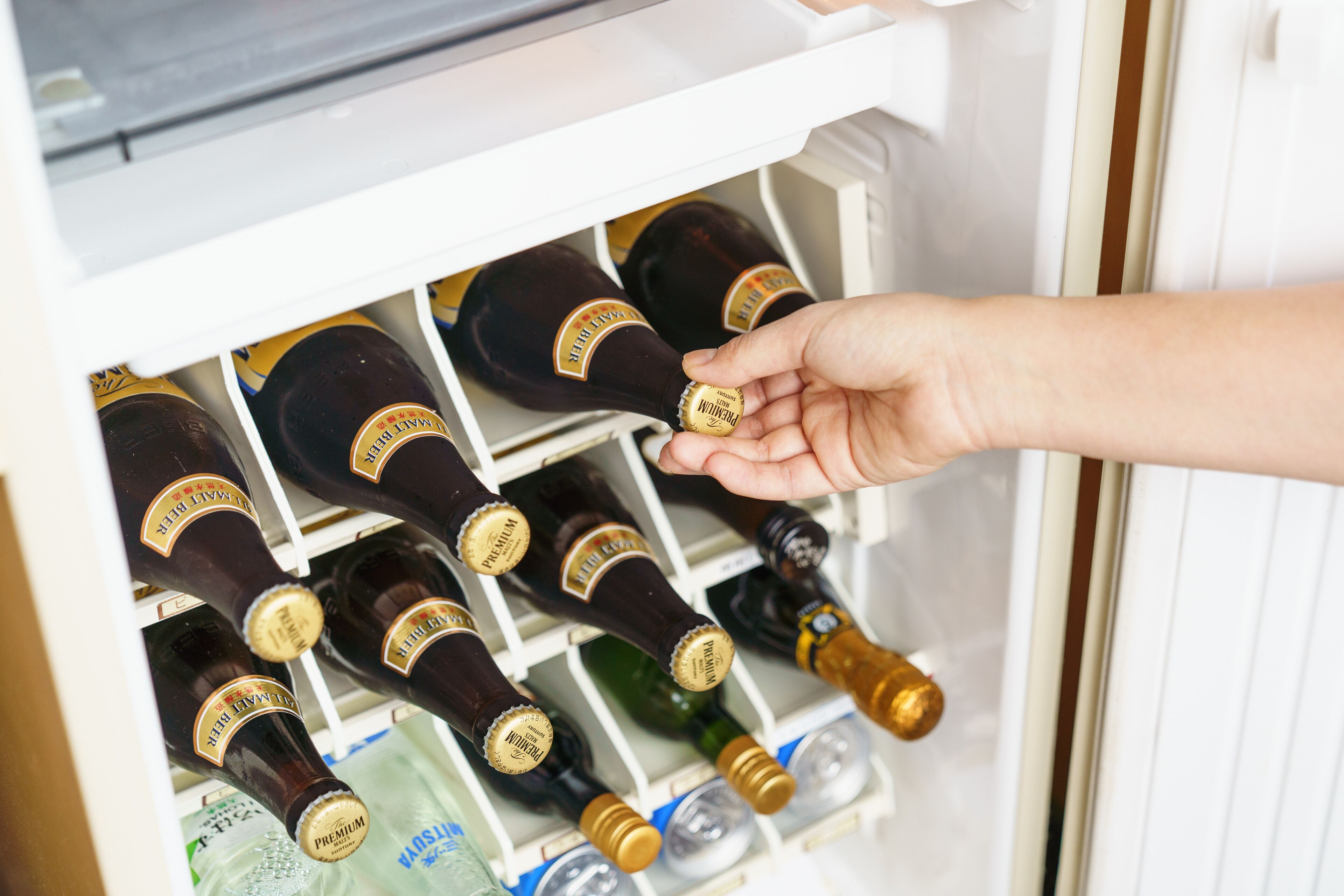 A hand reaching for a bottle in a refrigerator filled with various bottles.