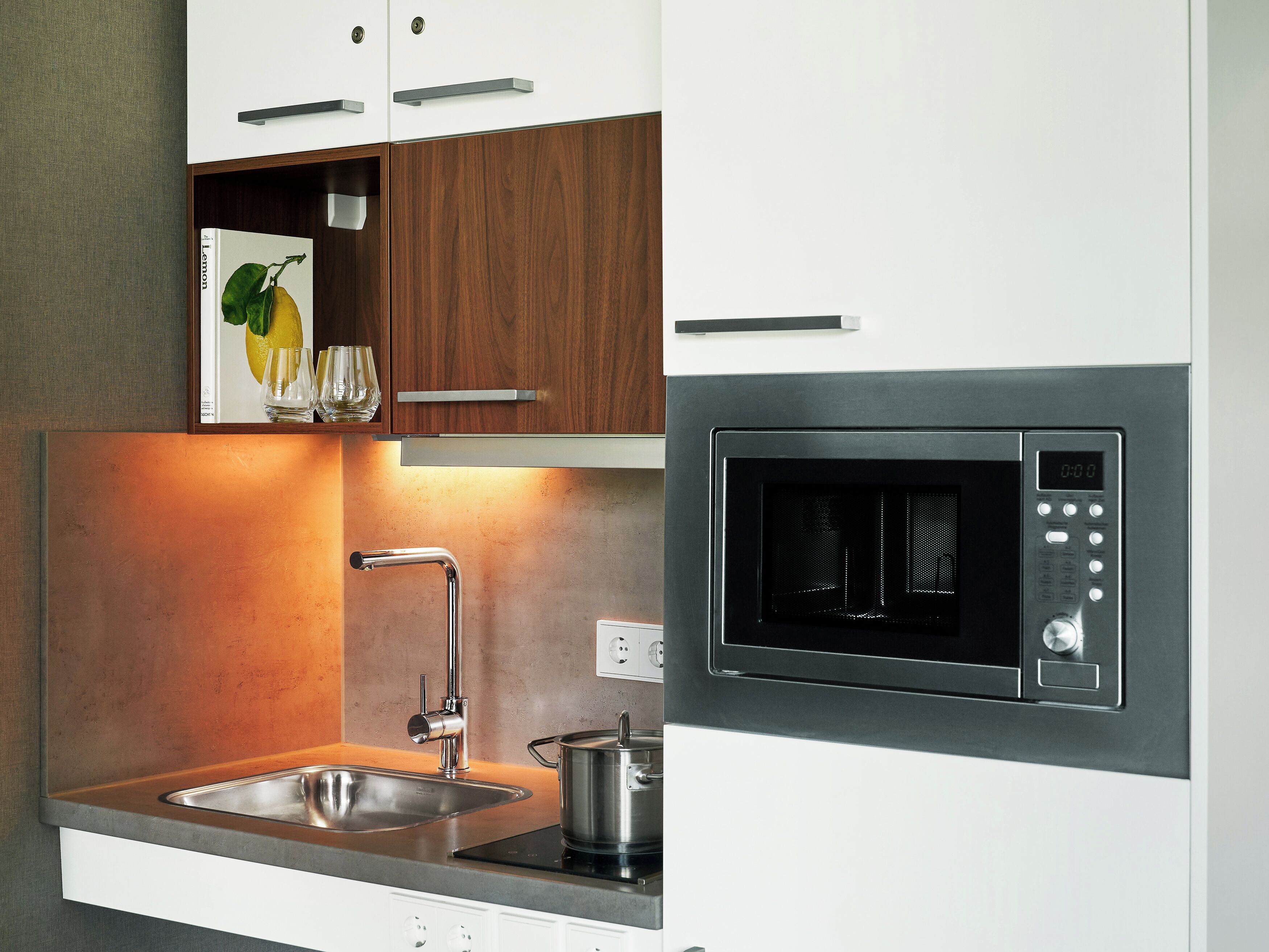 A modern kitchen with a built-in microwave, stainless steel sink, and wooden cabinets.