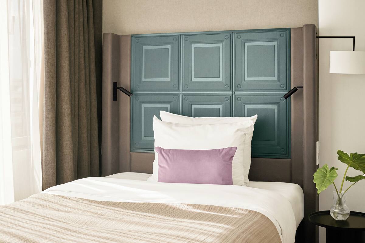 Une chambre d’hôtel avec un lit, une table de chevet, une lampe et une fenêtre avec des rideaux.