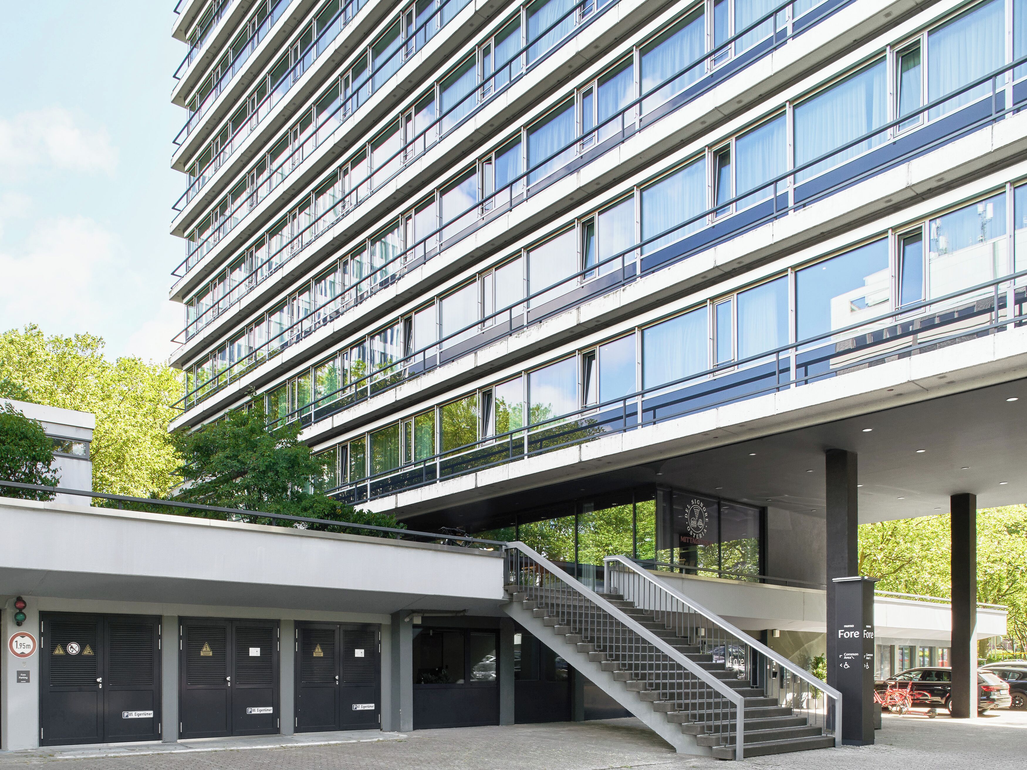 A modern building with multiple floors, large windows, and a covered entrance with a staircase.
