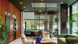 Un hall d’entrée moderne avec un comptoir d’accueil en bois, un espace salon et de grandes fenêtres donnant sur l’extérieur.
