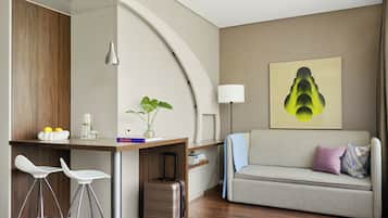 Ein modernes Hotelzimmer mit einer Küchenzeile, einem Sofa, einem Essbereich mit Barhocker und einem großen abstrakten Gemälde an der Wand.
