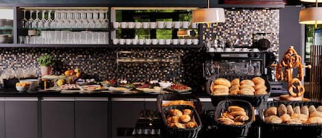Un bufé de desayuno con diversos alimentos, una máquina de café y un panel con los precios de la comida.