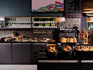 Een ontbijtbuffet met diverse gerechten, een koffieapparaat en een bord waarop de prijzen staan vermeld.