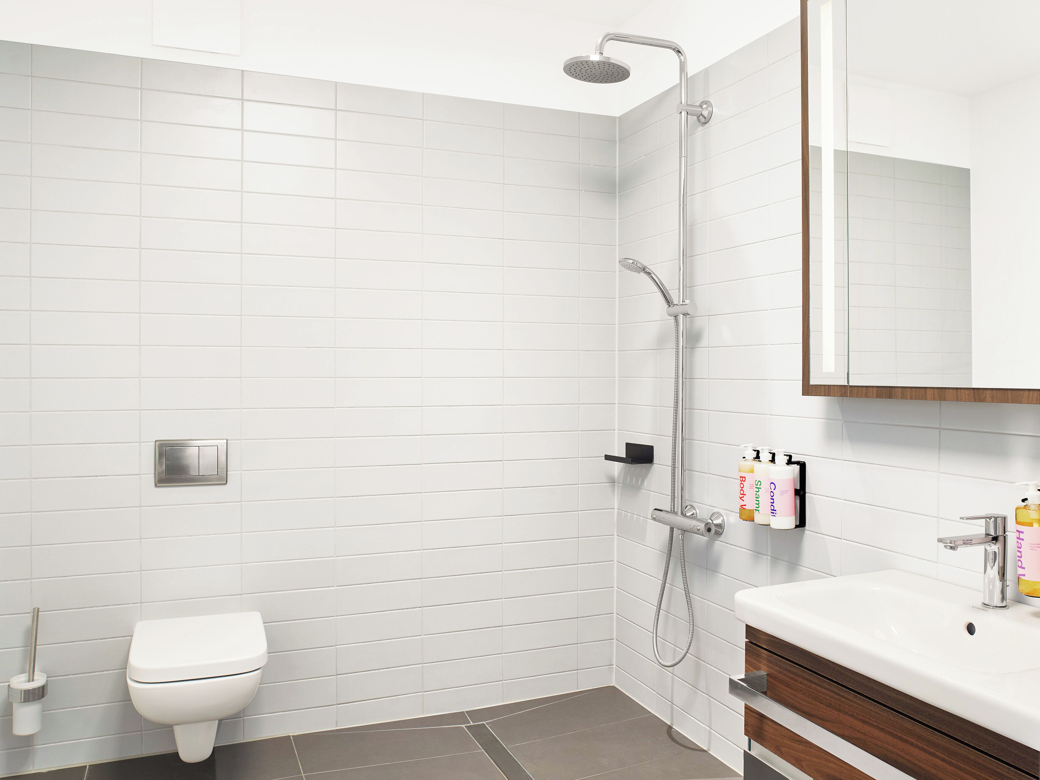 A modern bathroom with white tiles, a shower, a toilet, and a vanity with a mirror.