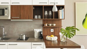 Une cuisine moderne avec des armoires blanches, un plan de travail en bois, un four à micro-ondes encastré, une machine à café et une plante en pot.