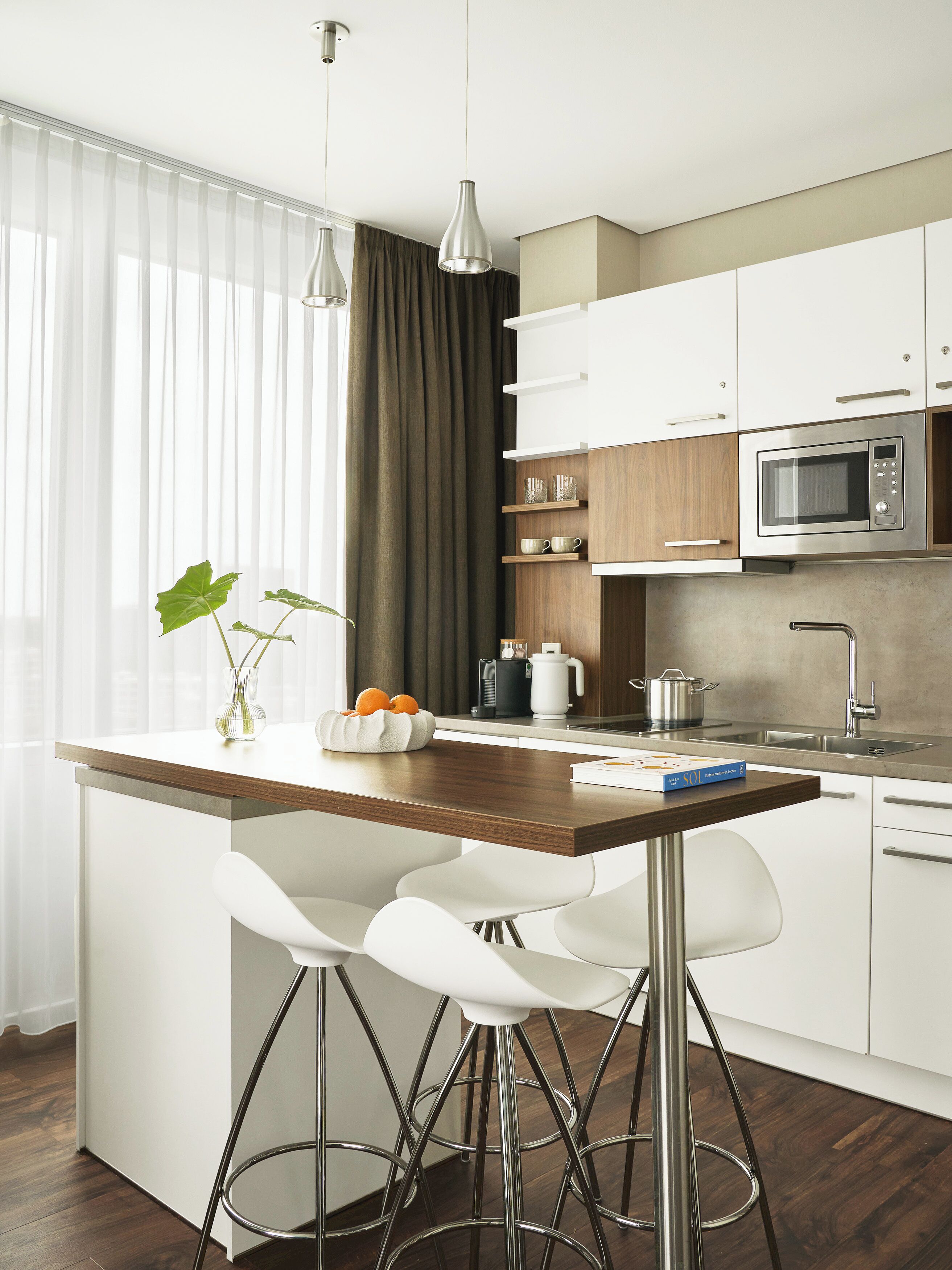 A modern kitchen with white cabinetry, a wooden island, stainless steel appliances, and a bar stool.