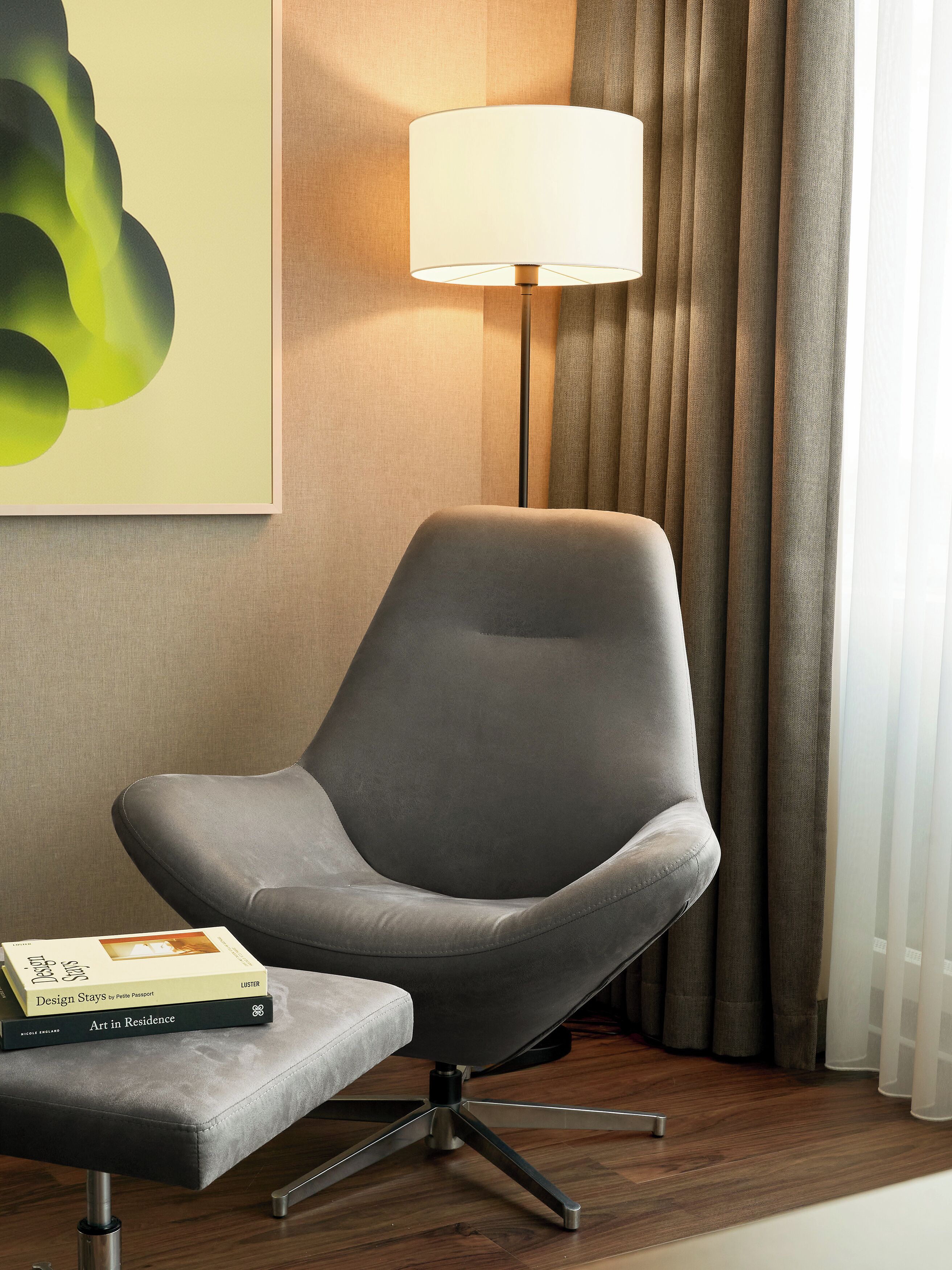 Un fauteuil moderne doté d’un socle métallique, placé à côté d’une petite table sur laquelle repose un livre intitulé « Design Stays by Pete Passport ».
