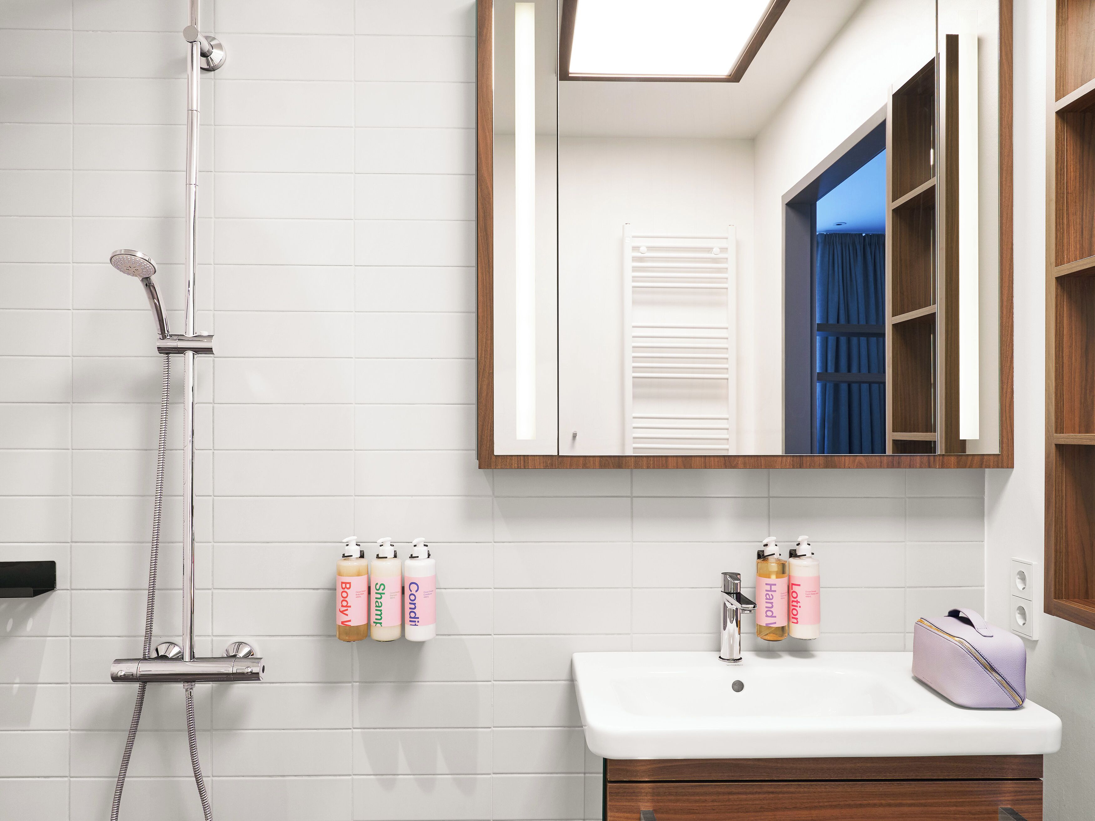 A bathroom with a shower, a sink, and a mirror. There are toiletries on the wall and a towel rack.