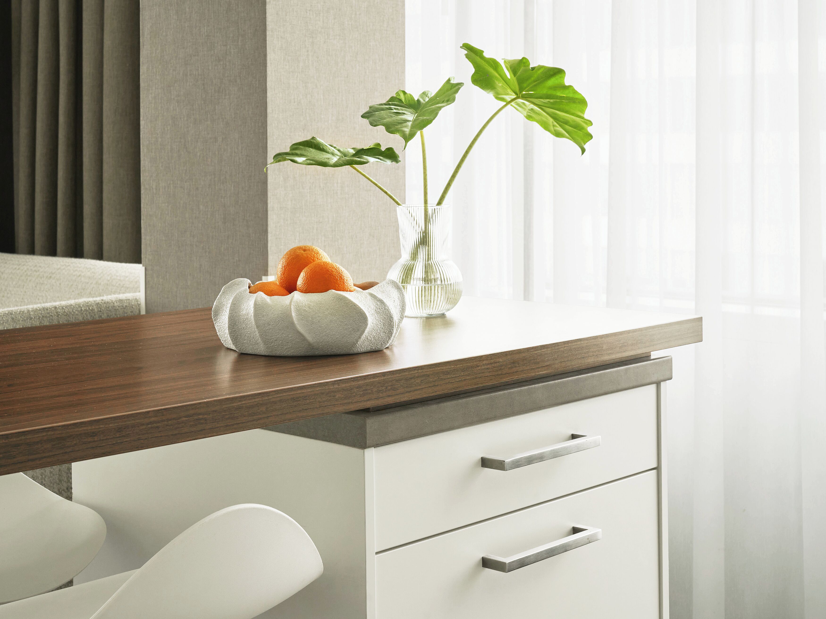 Una cocina moderna con encimera de madera, armarios blancos y un florero con hojas verdes y naranjas.
