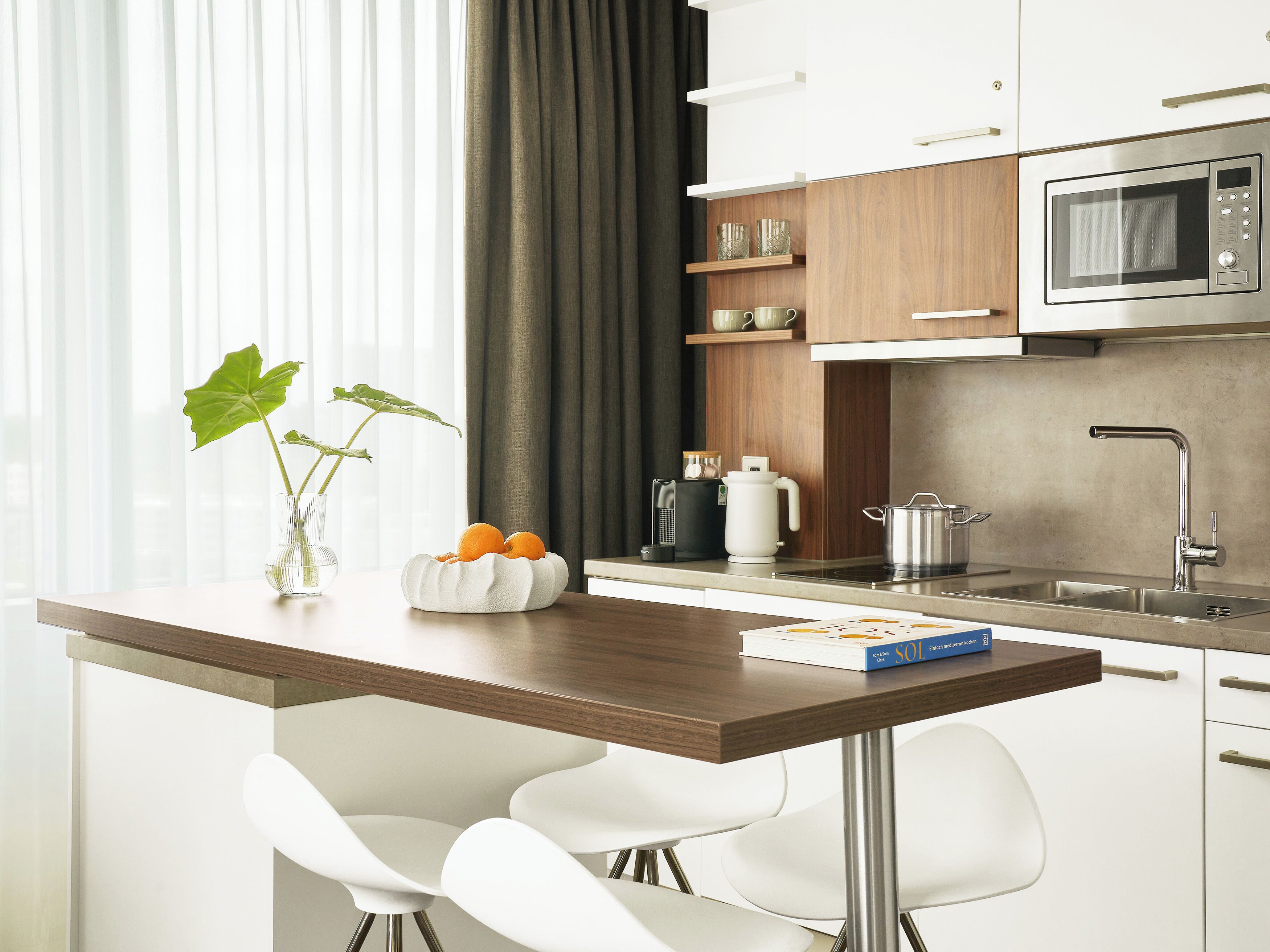 A modern kitchen with a wooden countertop, white chairs, a microwave, and a coffee maker.