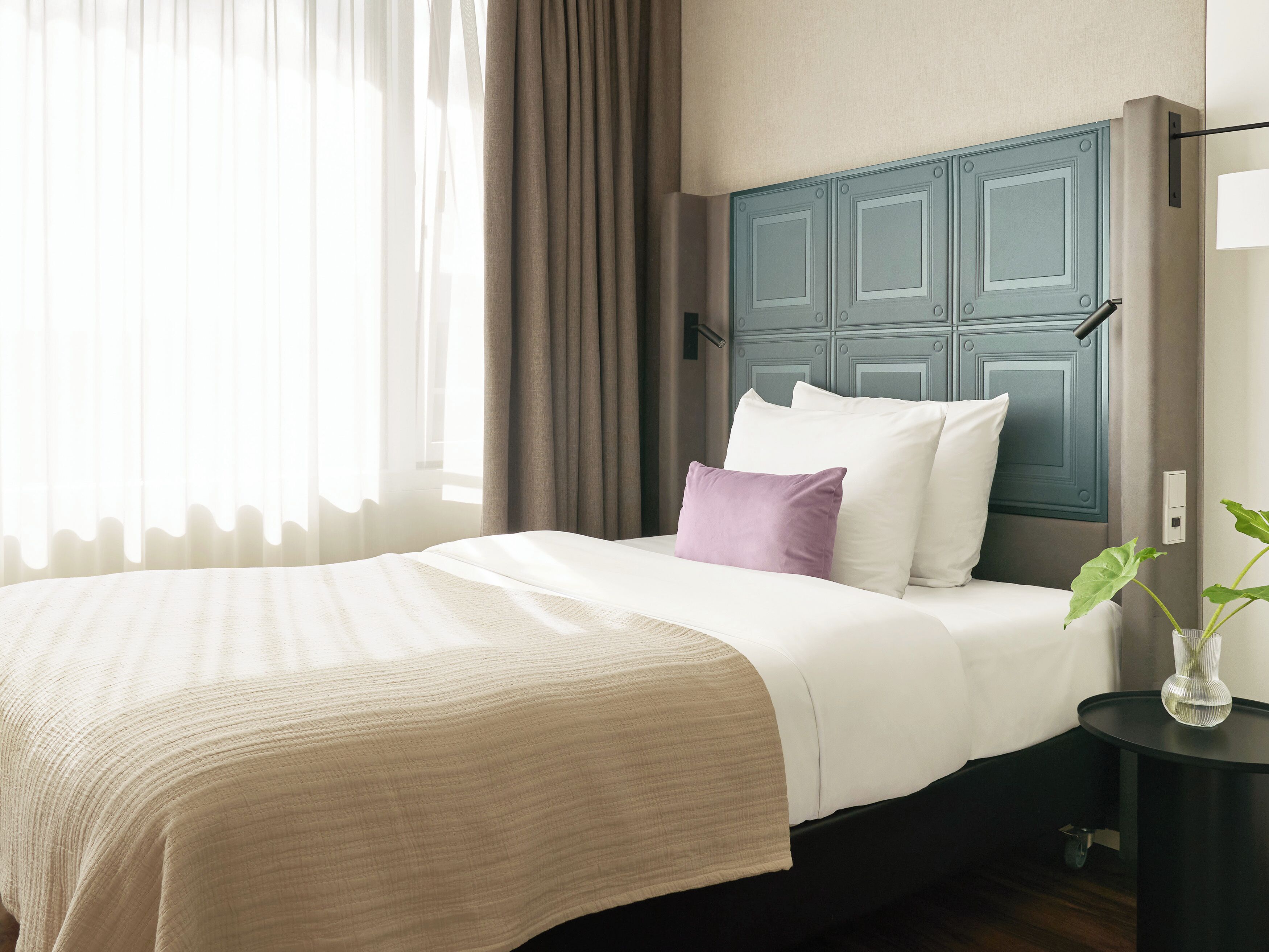 A neatly made bed with a beige bedspread, a white pillow, and a purple pillow.
