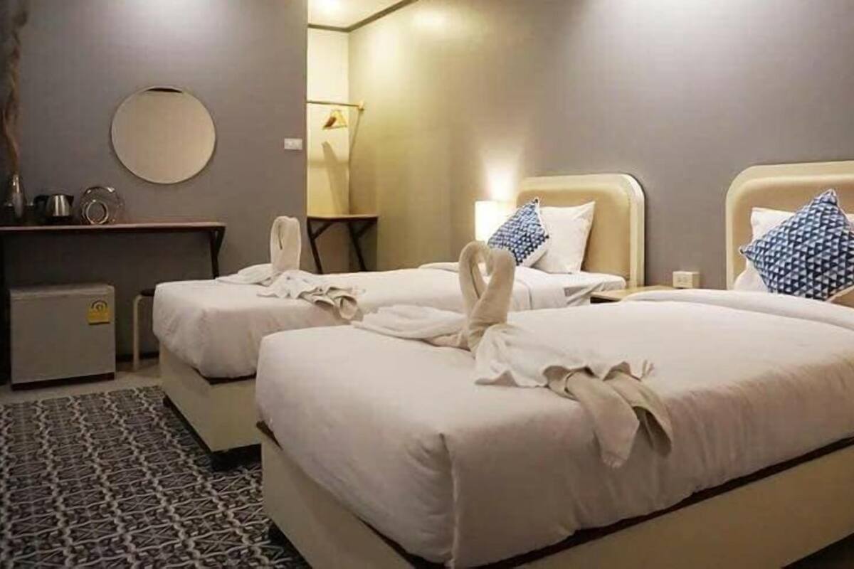 Une chambre d’hôtel avec deux lits, un miroir rond, une petite table et un tapis à motifs.
