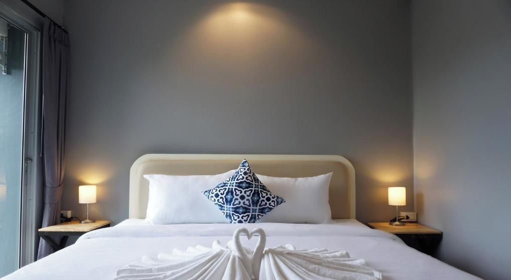 Une chambre d’hôtel avec un lit, deux lampes de chevet, un coussin décoratif et une serviette pliée en forme de cœur.