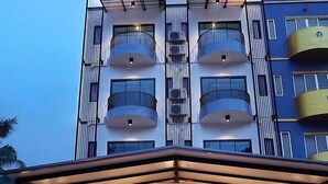 A multi-story hotel with a modern design, featuring balconies on each floor, a covered entrance, and a stone facade.