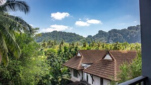 A view from a balcony overlooking a lush landscape with a house featuring a tiled roof and white walls.