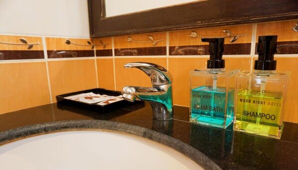 Un lavabo de salle de bain avec un robinet chromé, deux flacons de shampoing de la marque Moon Night Hotel et un petit plateau avec un savon.