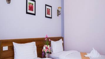 Habitación de hotel con dos camas, ropa de cama blanca, cabecera de madera, un jarrón con flores y cuadros en la pared.
