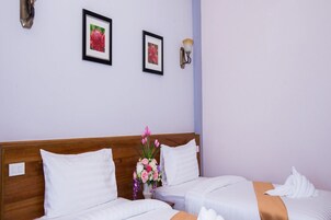 Habitación de hotel con dos camas, ropa de cama blanca, cabecera de madera, un jarrón con flores y cuadros en la pared.