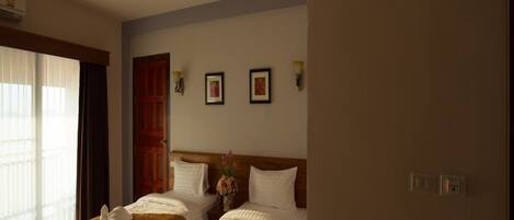 Habitación de hotel con dos camas, cabecero de madera, ventana con cortinas y lámpara fijada a la pared.