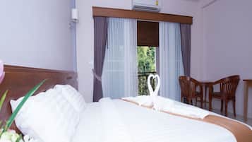 Habitación de hotel con una cama grande, cabecera de madera, balcón con vistas y una pequeña mesa con sillas.