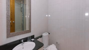 Un baño con lavabo blanco, espejo con marco decorativo, ducha e inodoro.