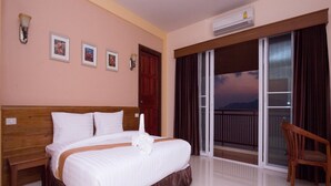 Una habitación de hotel con una cama grande, cabecera de madera, una silla de madera, un balcón con vistas y un aire acondicionado.